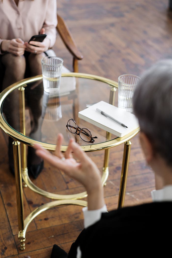 our-story-01 Two adults engaged in a therapy session, seated at a glass table with notebooks and water glasses.